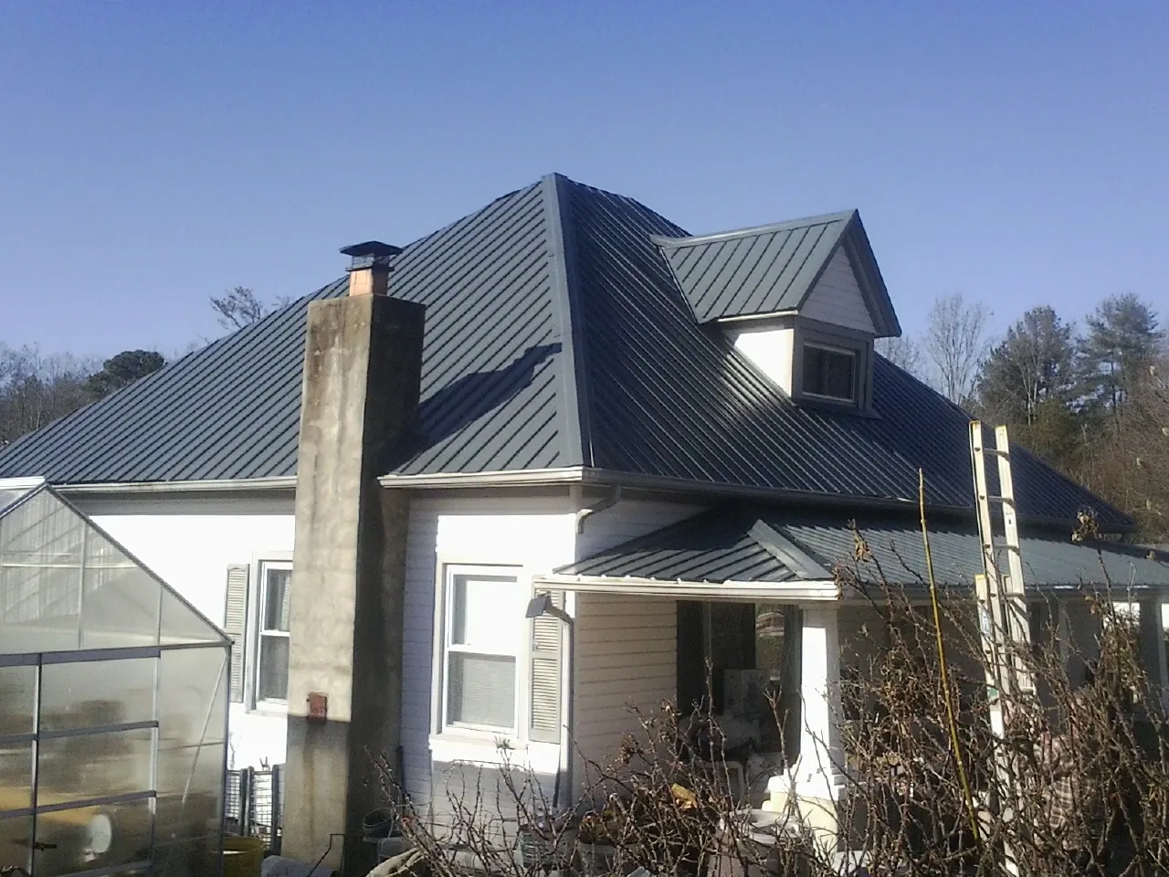 Dark blue standing seam metal roof on a white farmhouse with dormer — Slate & Tile Roof Repair by Roofing Brothers in Muscoda
