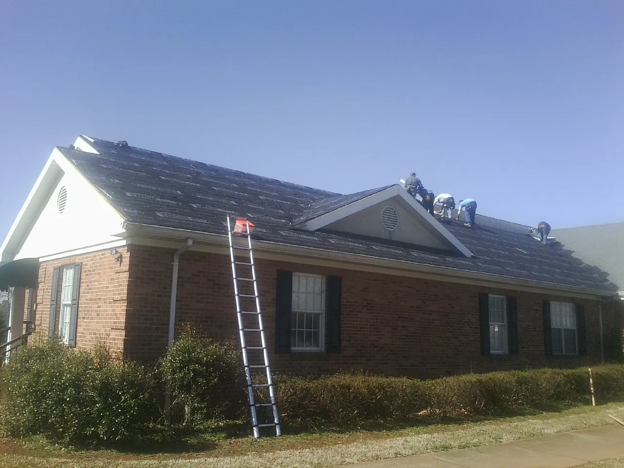 Crew tearing shingles off a brick ranch roof with a ladder set — Emergency Roof Repair work by our crew in Muscoda