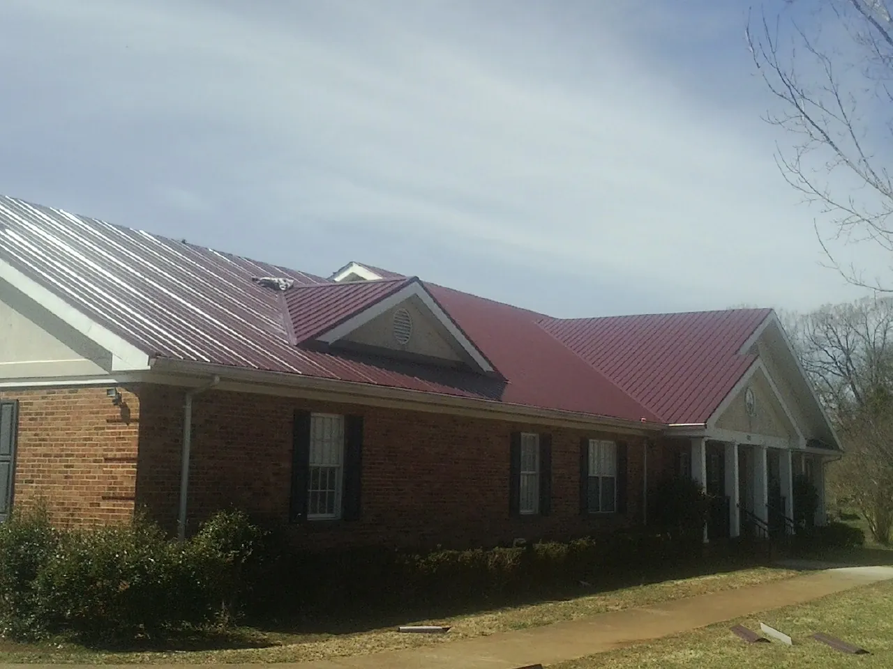 Red metal roof with gabled entries on a long brick building, from a Hail Damage Roof Repair job in Muscoda