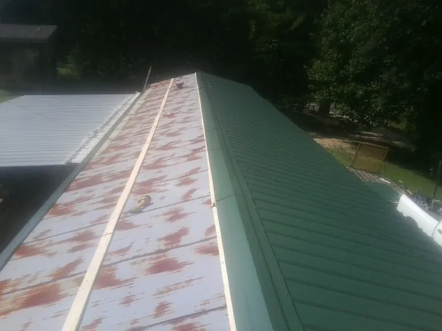 Old rusted panels beside newly installed green metal roofing — Wind Damage Roof Repair by Roofing Brothers in Muscoda