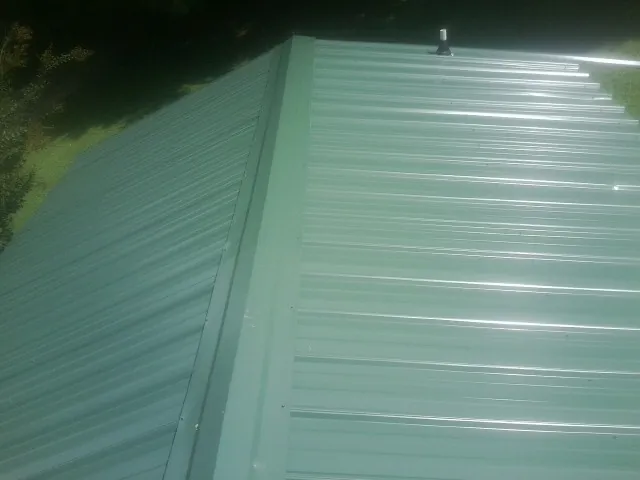 New green metal panels meeting at the ridge of a roof — Flat Roof Repair work by our crew in Muscoda