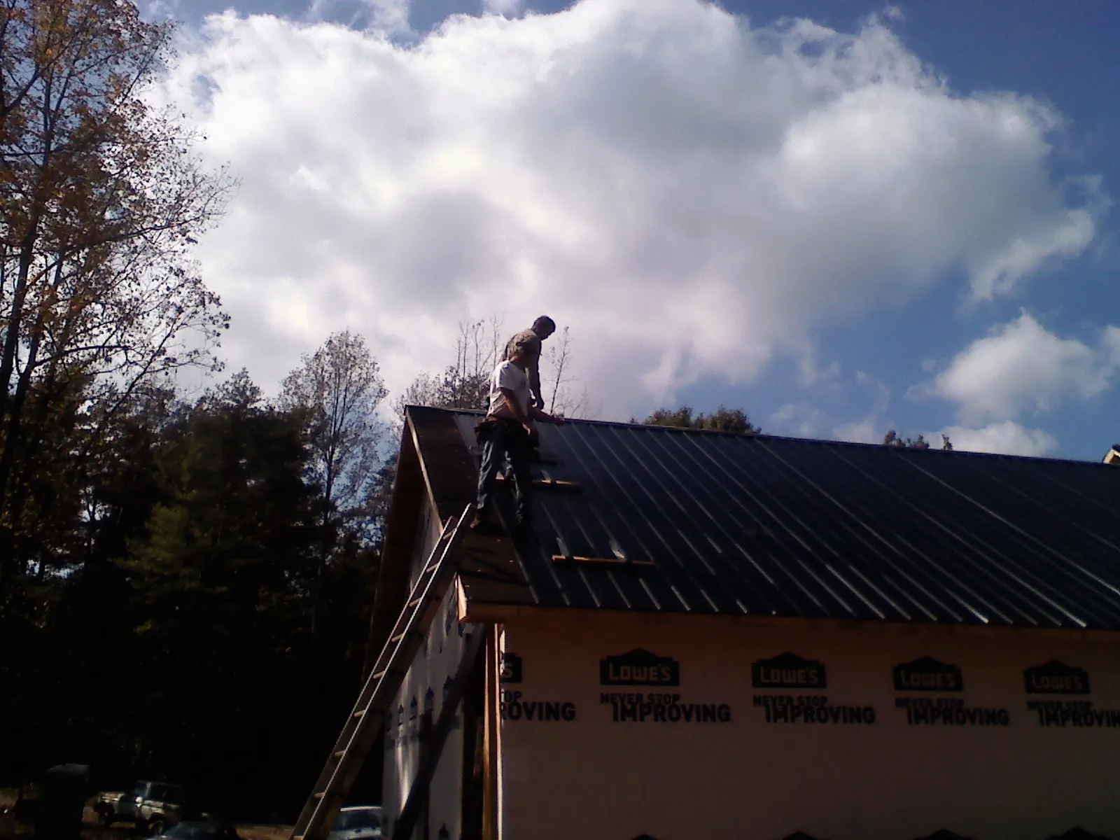 Roofer fastening dark metal panels high against a cloudy sky, from a Roof Inspection job in Muscoda
