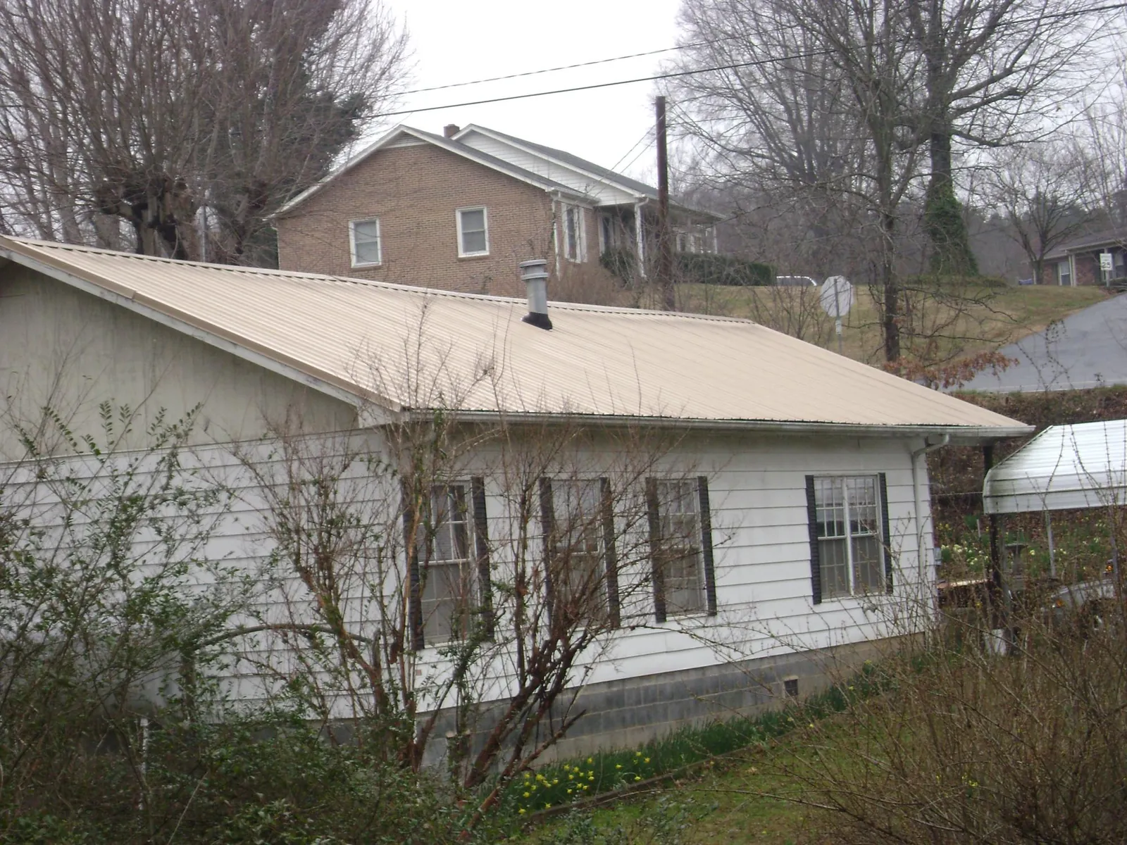 Tan metal roof on a white sided house set into a hillside — Commercial Roofing by Roofing Brothers in Muscoda
