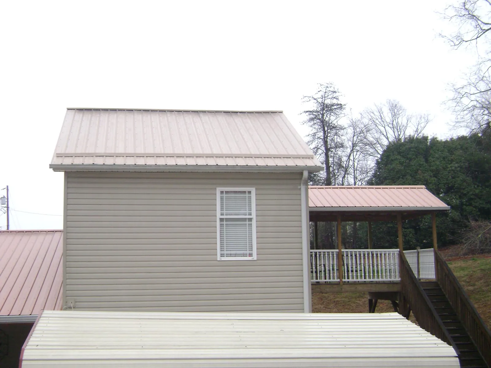 Tan metal roofs on a two story addition and attached porch, from a Roof Replacement job in Muscoda